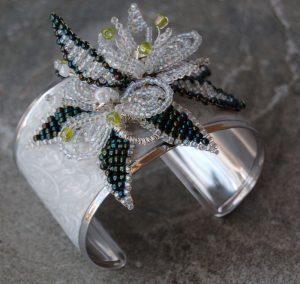 Metal bracelet with beaded flower and butterfly design.