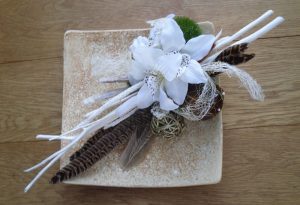 Contemporary silk flower design on ceramic dish with orchids and feathers.